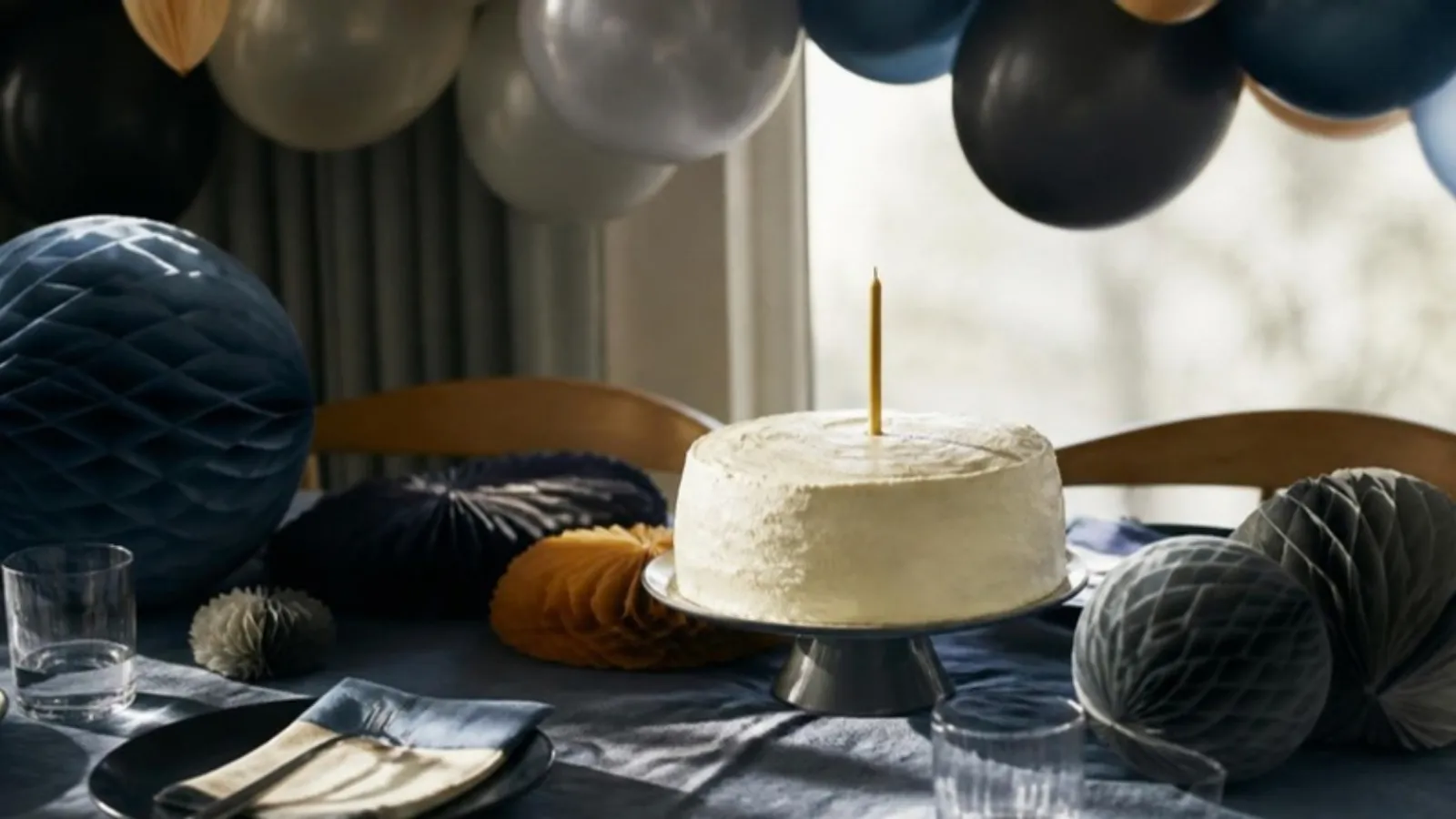 Tisch mit Luftballons und Papierdeko um einen Kuchen mit einer Kerze